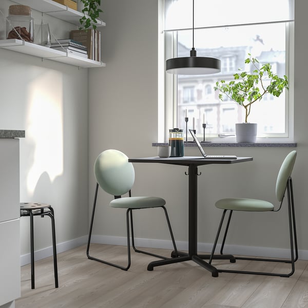 Modern kitchen nook with black metal STENSELE table and green cushioned chairs, perfect for small spaces.