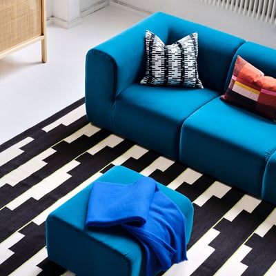 Bright blue modular sofa on black and white geometric rug, includes two colourful pillows.