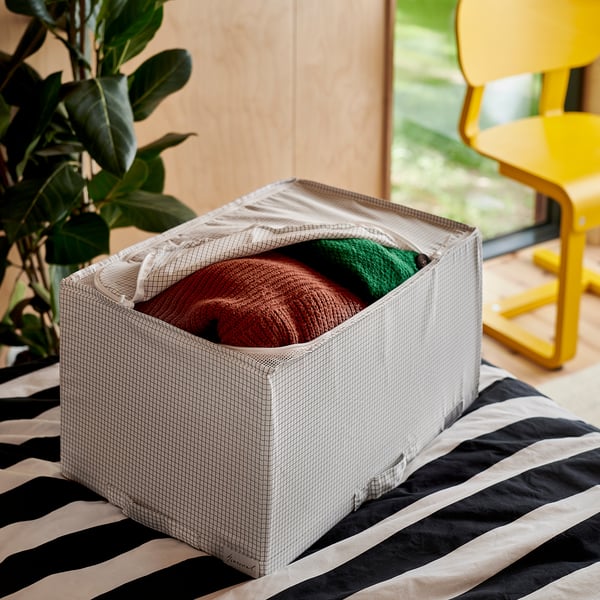 Storage box holding folded blankets, placed on black and white striped fabric.