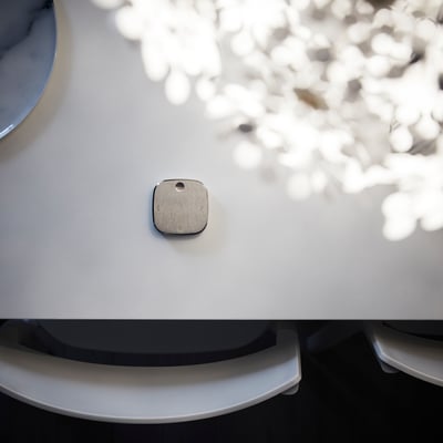 Small, square, metallic button on a white surface, likely a remote control.