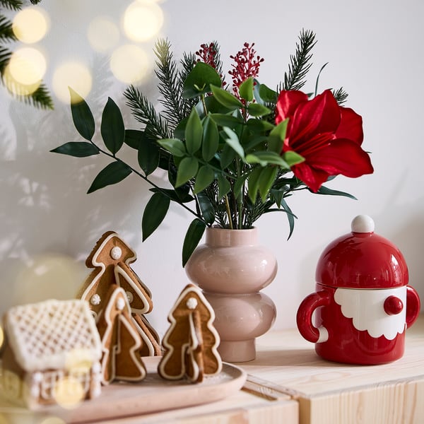 Christmas-themed display with red santa mug, gingerbread cookies, and pink vase with green and red flowers.