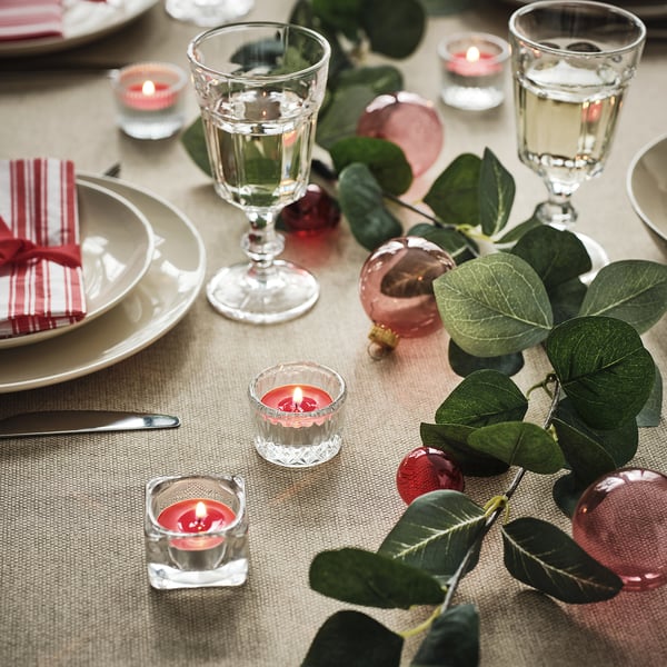 Elegant dinner table with VINTERFINT tealights, red candles, leaves, ornaments, and dinnerware, creating a cosy, festive atmosphere.