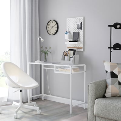 VITTSJÖ laptop table with glass top, metal frame, wall-mounted pegboard, white chair, grey sofa with pillows.