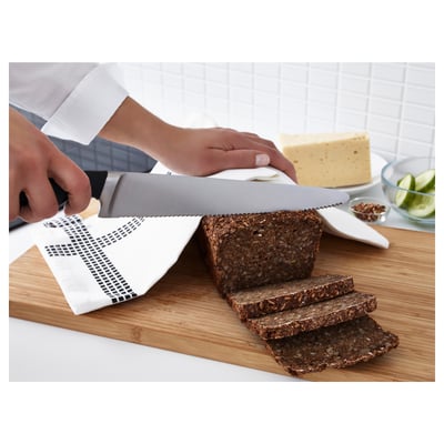 Person slicing bread with a serrated knife on a wooden cutting board beside a cheese and lime bowl.