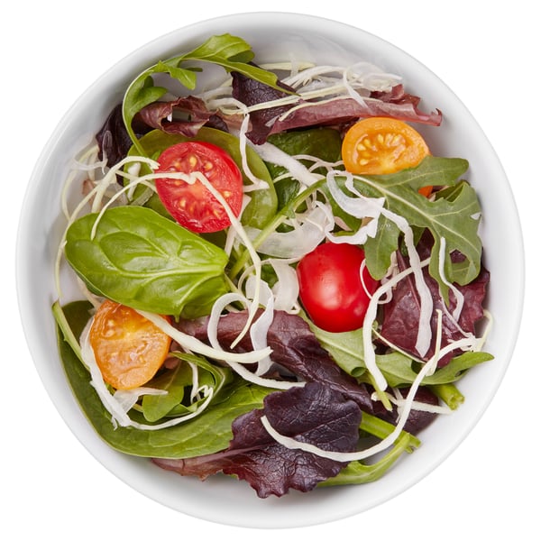 Fresh salad in white bowl, topped with tomatoes, onions, spinach, and assorted greens.