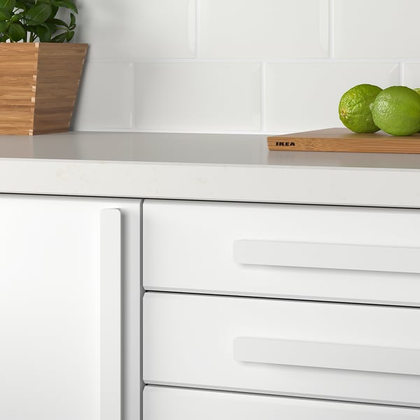 White kitchen drawers with modern handles. Limes on wooden board, plant in background.