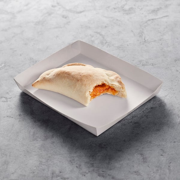 A hand-held baked pastry with a tomato filling, placed in a cardboard container on a stone surface.