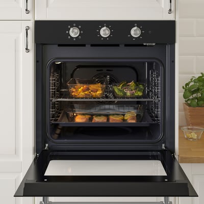 Black oven with glass door open, showing dishes inside, placed in two racks. Controls on top, set in a modern kitchen.