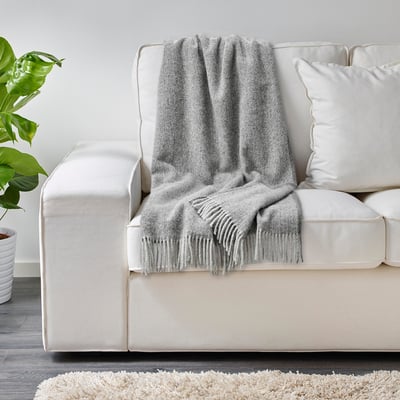 Grey wool throw blanket on white couch, providing cozy warmth and soft touch.