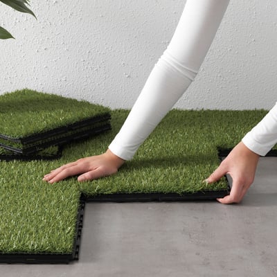 Person assembles RUNNEN outdoor grass tiles. Easy to connect for cosy balconies or terraces.
