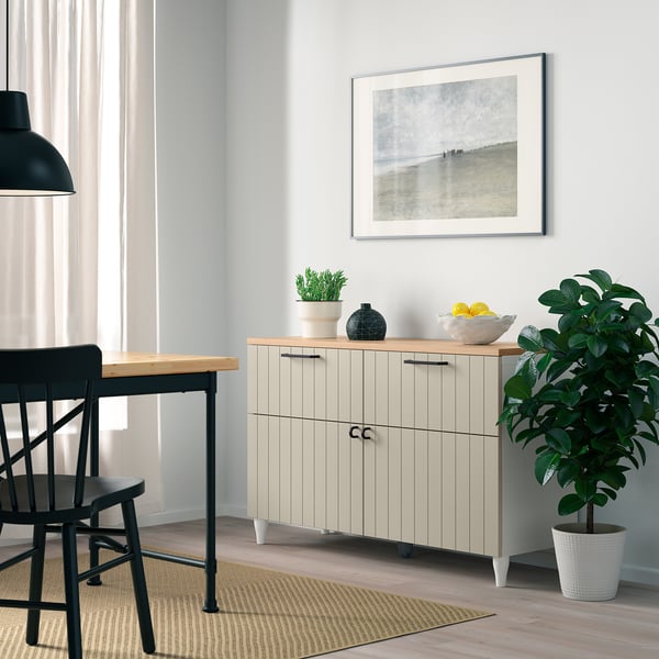 Modern living room with beige BESTÅ sideboard, black chairs, gray photo, plant, and fruit bowl.