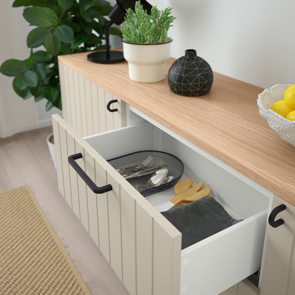 Open drawer reveals utensils, black handles, white cabinet, wood top.