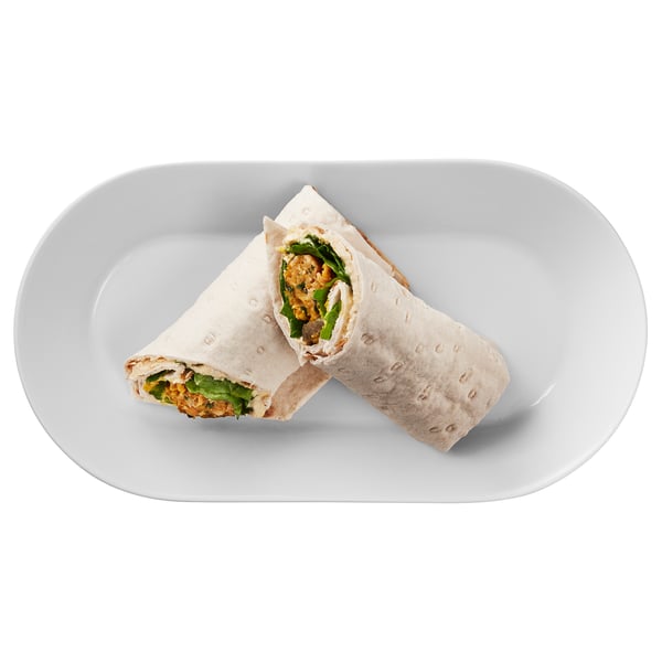 A wrap cut in half on a plate. Contains greens and grain.