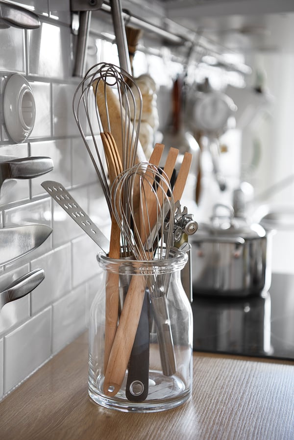 Wooden and stainless utensils in glass jar on counter