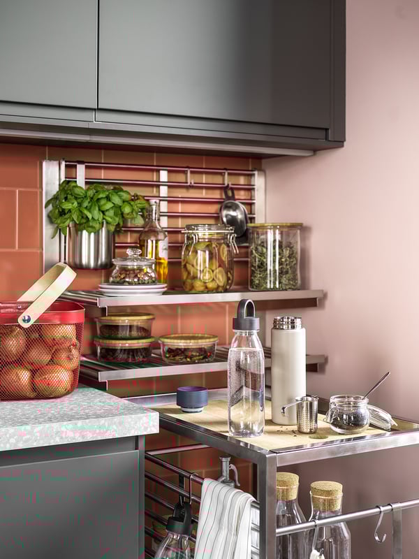 Современная кухня с серыми шкафами, розоватыми стенами, загроможденной столешницей и открытыми полками с продуктами питания.