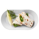 Ein Tortilla-Wrap mit Gemüse auf einem weißen Teller, garniert mit Zitrone und Dill.