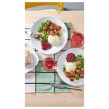 Twee borden met gehaktballen, aardappelpuree, erwten en jam; Vorken en messen op groene doek.