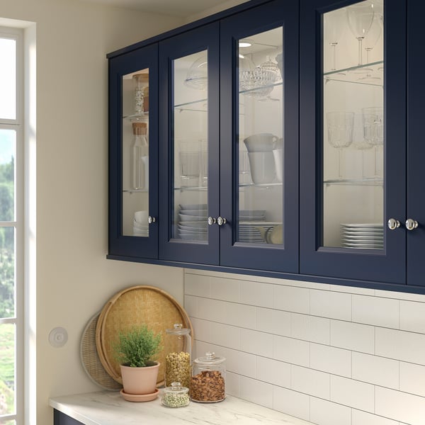 Modern kitchen with blue glass cabinetry, plant, snacks, and white backsplash.