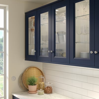 Modern kitchen with blue glass cabinetry, plant, snacks, and white backsplash.