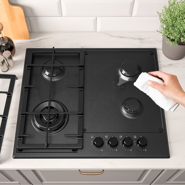 A hand cleans a modern black gas stove with four burners using a cloth. The stove sturdy cast iron supports and electronic ignition.