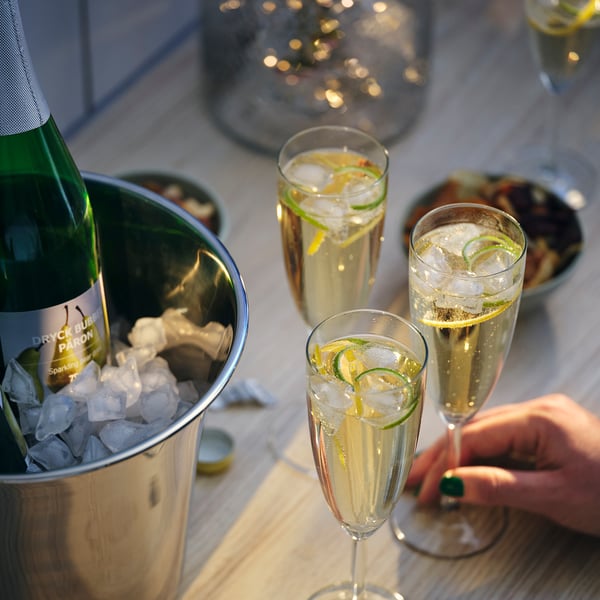 Image a metallic ice bucket with green bottle labeled DRYCK BUBBEL PÄRON and glasses of sparkling drinks with lemon and lime slices.