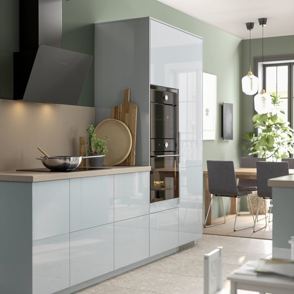 Modern kitchen with white cabinets, black hood, and stainless steel oven. Light green walls, pendant lights, and a dining area with chairs.
