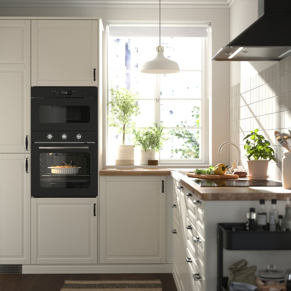 Modern kitchen with cream cabinets, black oven, wooden countertop, potted plants, and a window with a city view.