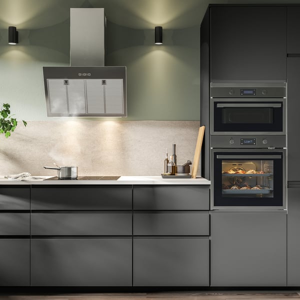 Modern kitchen with black cabinets, stainless steel range hood, built-in oven, and countertop items.