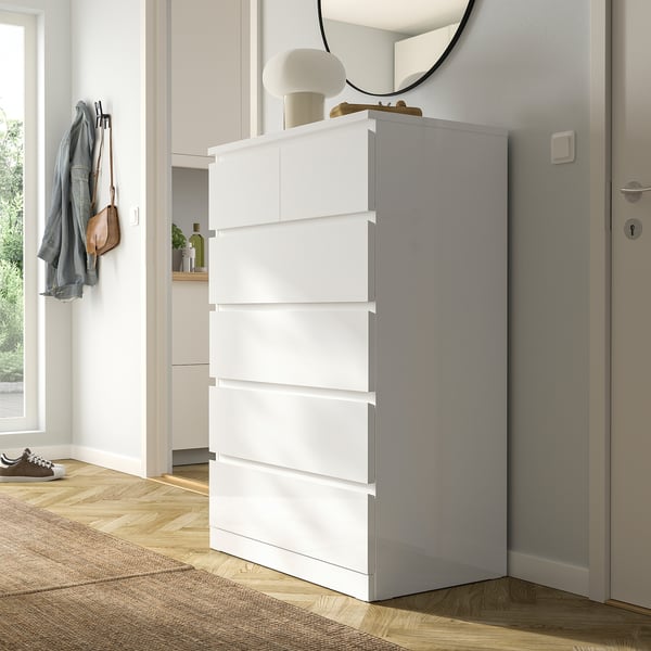 White MALM chest with 6 drawers, slightly open top, lamp, mirror, modern decor.