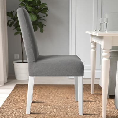 A modern dining chair with a gray upholstered seat and back, white legs, and a clear glass on a white wooden table nearby, perfect for dining rooms.