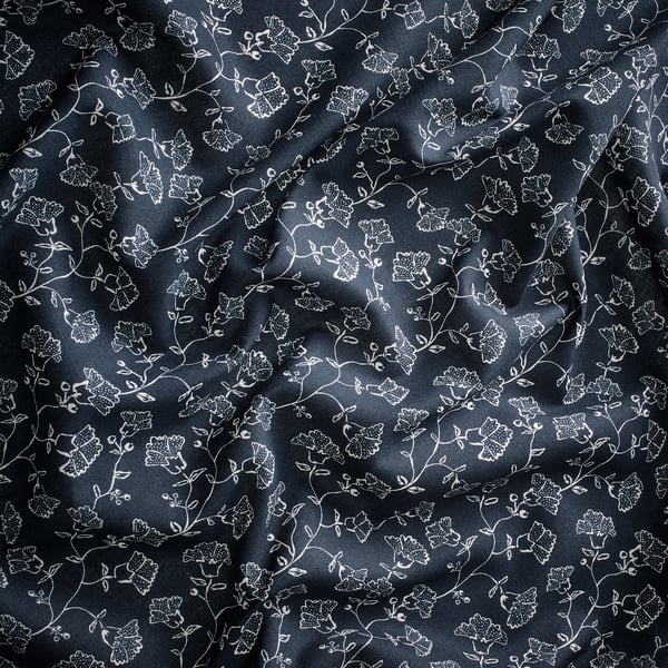 Темно-синяя штора с белым цветочным узором, предлагающая мягкую, нежную драпировку, улучшающую декор комнаты.