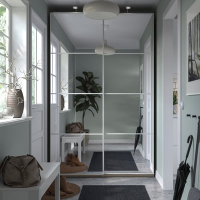 Modern entryway with PAX wardrobe, mirrored sliding doors, gray rugs, white walls, pendant lights, and potted plants.