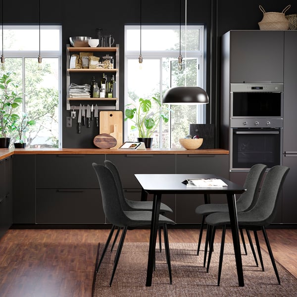 Modern kitchen with black GALLERUD chairs. Dark wood floor, large windows, and built-in oven. Chairs small, fitting under rectangular table.