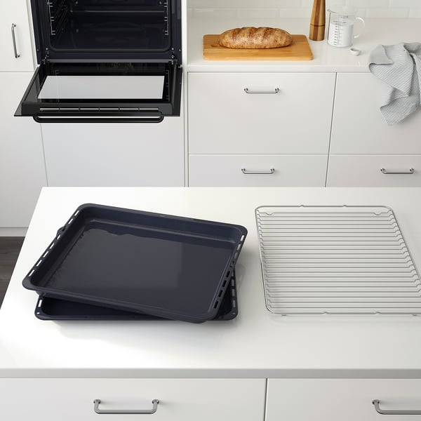 Oven open, displaying baking trays. Countertop shows baking tray and cooling rack. Fresh bread and kitchen tools nearby.