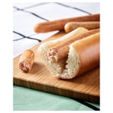 Hot-dog shaped plant-based food on a wooden board. Golden-brown exterior, soft interior. Placed on green cloth.