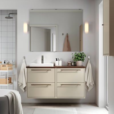 Modern bathroom with beige HAVBÄCK vanity and sink, two drawers, mirrored cabinet, and wall lamps. Towels hang beside it.