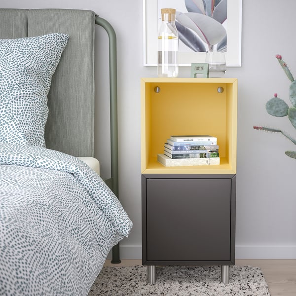 Small yellow and black EKET bedside cabinet with books, next to a grey bed with patterned bedding and a cactus.