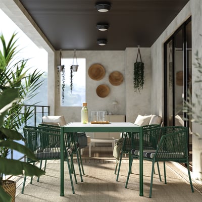 Modern outdoor patio with green metal chairs, glass table, hanging plants, and wall decor under a ceiling with spotlights.