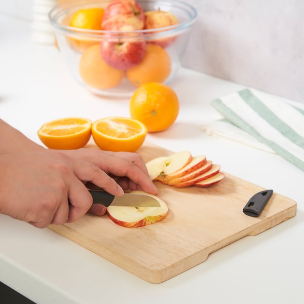 Person slicing apple with knife on cutting board, fruit in background
