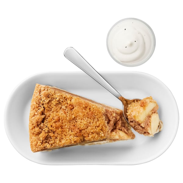Slice of apple crumb pie with cinnamon, cream on side. Served on a white plate with a spoon.