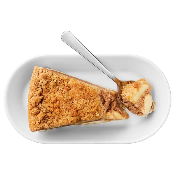 Image shows a slice of cinnamon crumb cake on a white plate with a spoon. The cake has a crumb topping and a soft, apple-filled center.