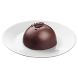 Round dark chocolate dessert on white plate, smooth texture, topped with chocolate shavings.
