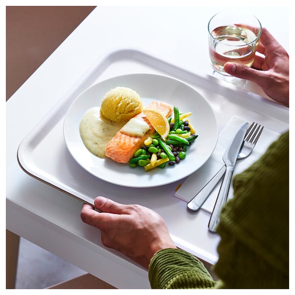 A meal with salmon, mashed potatoes, and vegetables on a white plate. Person wearing a green sweater, holding a glass.