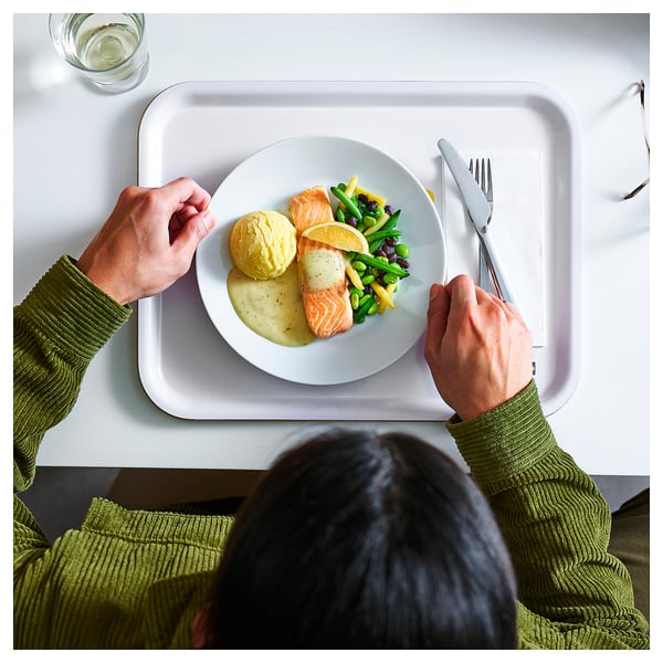Person in green sweater holding tray with meal and drink.