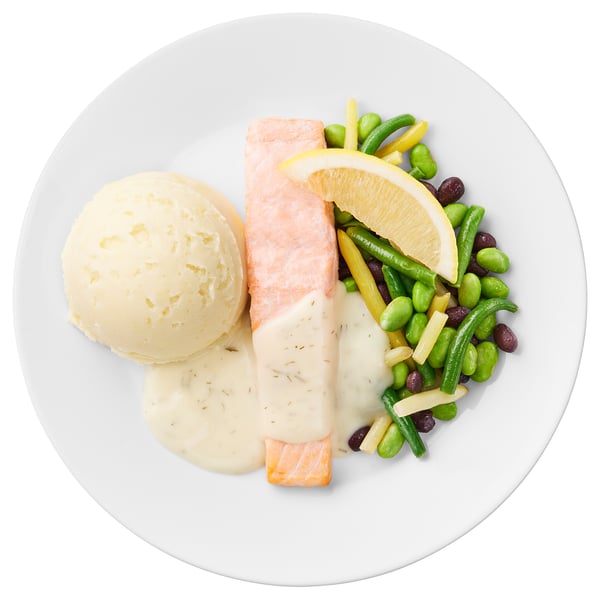 White plate with salmon fillet, mashed potatoes, and mixed vegetables including beans, peas, and corn. Garnished with lemon.