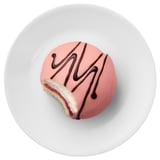 A pastry on a white plate with glazing and chocolate drizzle, half eaten.