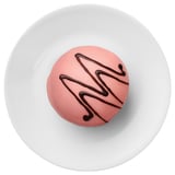 A single pinkish dessert sits on a white plate, decorated with a dark chocolate swirl pattern.