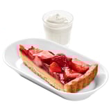 Image a strawberry tart with whipped cream on a white plate. Tart has a golden crust with fresh strawberries on top.