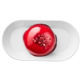 A round dessert with red glaze and raspberry pieces on a white plate.