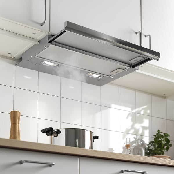 Stainless steel range hood embedded in white kitchen cabinet, illuminated with led lights, showing its extracted state.